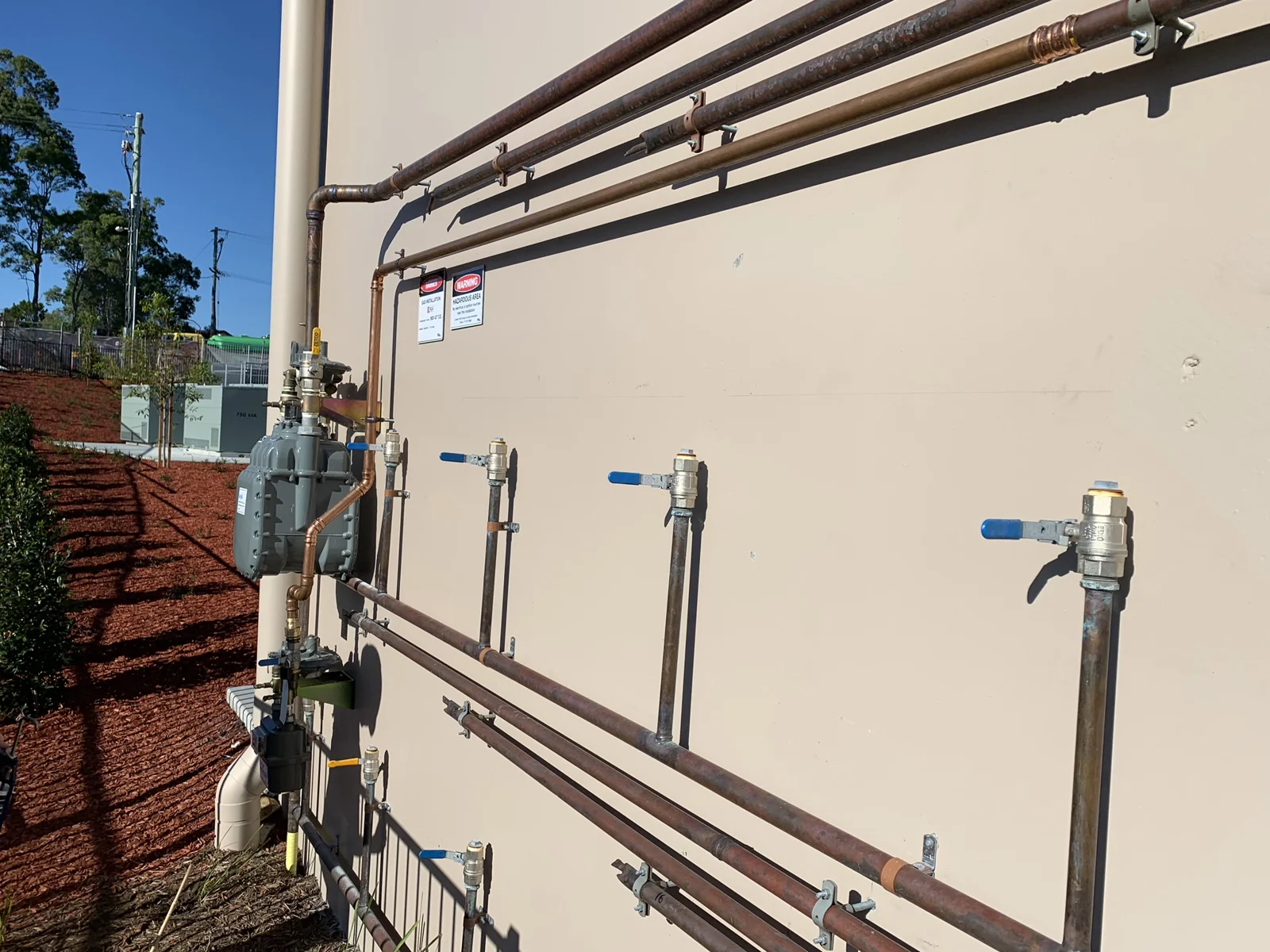 Copper gas pipework, meter and isolation valves with compliance signage on a Gold Coast gas installation