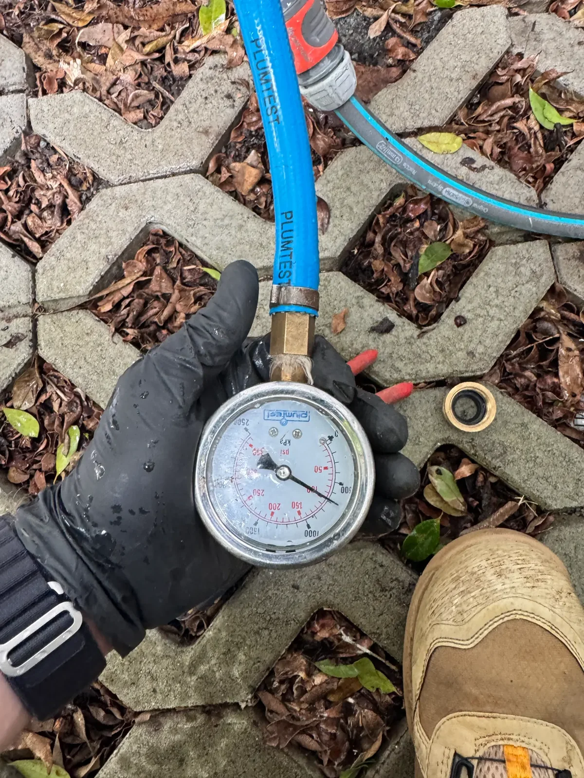 Gold Coast plumber holding a water pressure test gauge while checking for hidden leaks behind a high water bill