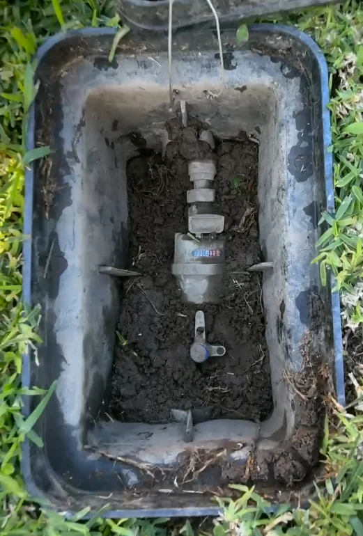 Water meter in a ground-level meter box being checked for movement while diagnosing a slab leak at a Gold Coast home